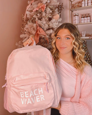 Image of Blonde model holding up pastel pink Beachwaver branded backpack