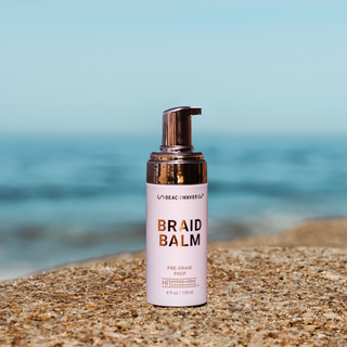 A pump bottle of Braid Balm hair care product placed on a stone surface with a blurred background.