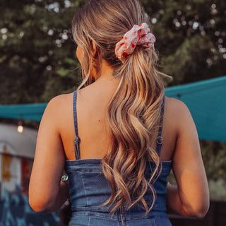 Image of model with brunette hair styled by Beachwaver hair tool pulled back in a oversize pink daisy scrunchie