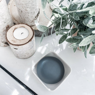 Image of Charcoal bar on bathroom counter in a soap dish surrounded by plants and candles.