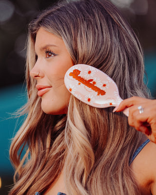 Image of brunette model using the On-Set Styling Brush that is pink with white and orange daisies on it.
