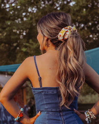 Image of model with brunette hair styled by Beachwaver hair tool pulled back in a oversize yellow daisy scrunchie