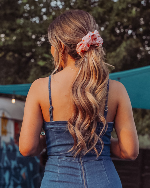 Image of model with brunette hair styled by Beachwaver hair tool pulled back in a oversize pink daisy scrunchie