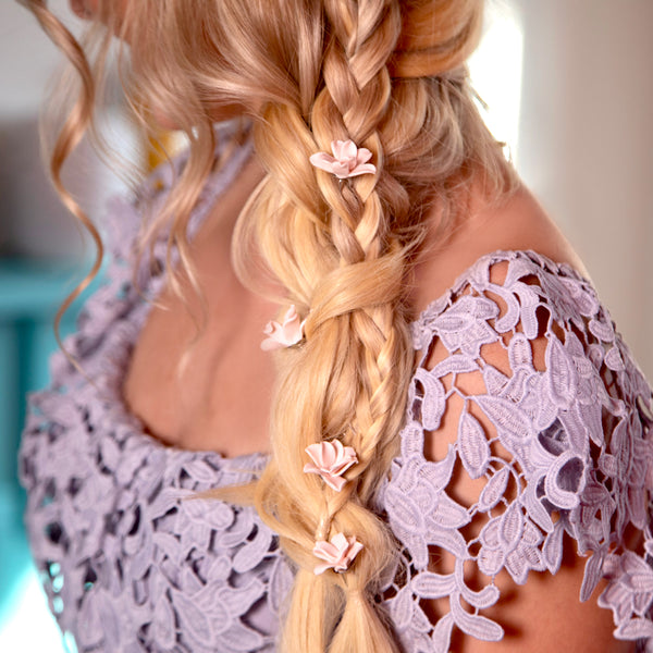 Image of model with long golden blonde hair styled in a braided fancy do with floral Hair pins placed throughout the braid