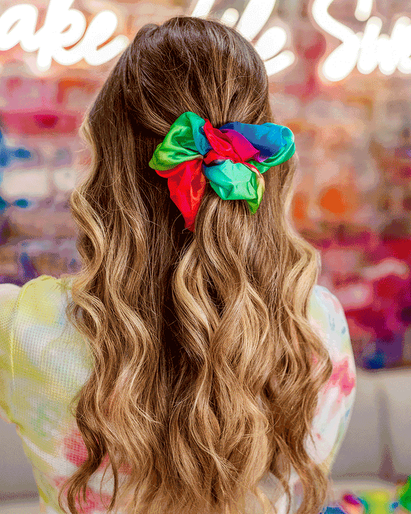 Gif of brunette model using the rainbow tie-dye oversize scrunchie to style hair multiple ways