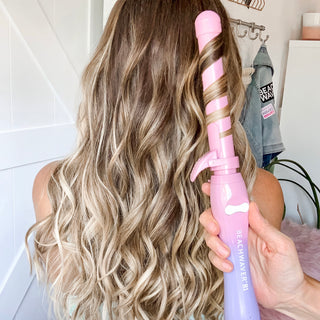Image of model with golden blonde hair and waves styled with the Beachwaver B1 Pink sunset that is in her hair.