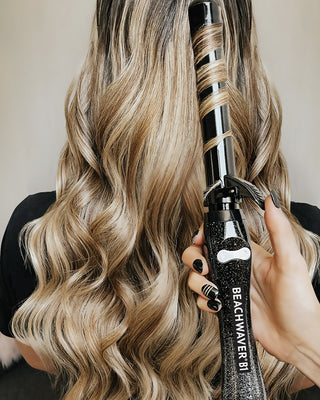 Image of model with long blonde hair that was styled by the black glitter Beachwaver B1 with the tool being held in her hair.