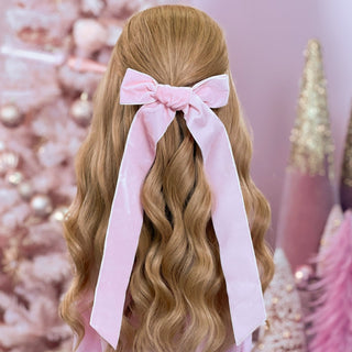 image of long golden hair styled in with a Beachwaver hair-tool pulled away from the face in a pink velvet bow.