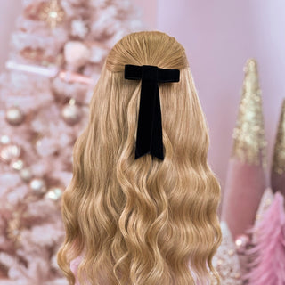 image of long golden hair styled in with a Beachwaver hair-tool pulled away from the face in a black velvet bow.