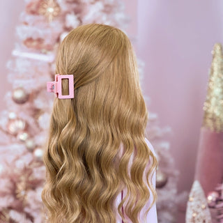 image of long golden hair styled in with a Beachwaver hair-tool pulled away from the face in a pink square Clawclip.