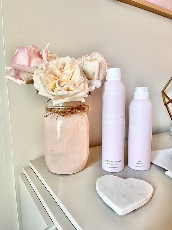 Image of Second Chance Dry Shampoo and Great Barrier Heat Protectant Hair Spray on a table next to pink flowers.