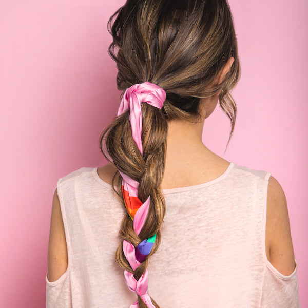 Image of brunette haired model with her long hair pulled back into a braid with a pink and rainbow hair scarf braided into it.