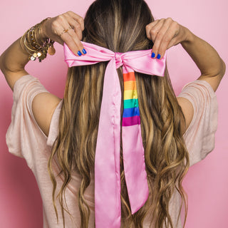 Image of brunette haired model with long hair styled by the beachwaver b1 love iron with her hair pulled away from her face with a pink silky hair scarf with a rainbow pattern on it.