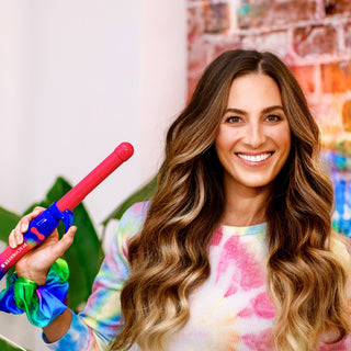 Image of brunette model with long styled hair holding up the pink and rainbow tie-dye B1 Beachwaver.
