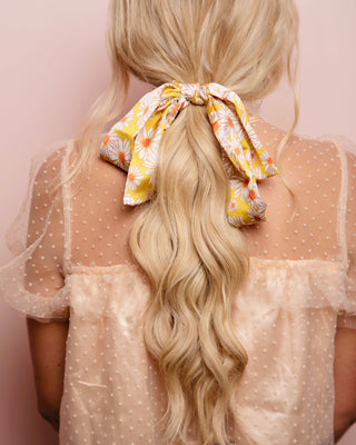 Image of blonde model with her hair styled by Beachwaver hair tool pulled away from face using a hair scarf that is yellow with white daisies