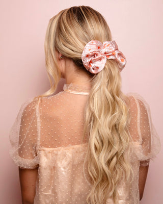 Image of model with blonde hair styled by Beachwaver hair tool pulled back in a oversize pink daisy scrunchie