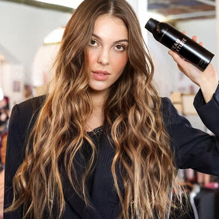 Image of Brunnet Model with long wavey hair holding  up the team texture spray that was used on her hair.
