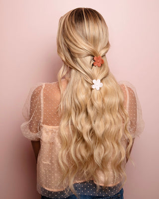 Image of blonde model with long hair styled by Beachwaver hair tool pulled away from her face using a pink and orange daisy clip